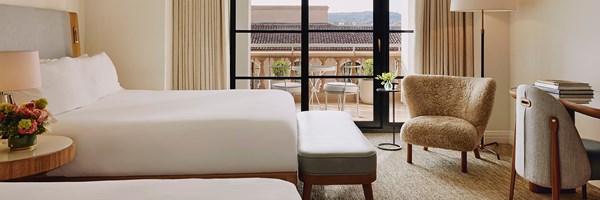 Hotel room with two queen beds, a desk and chair with a terrace with seating for two.