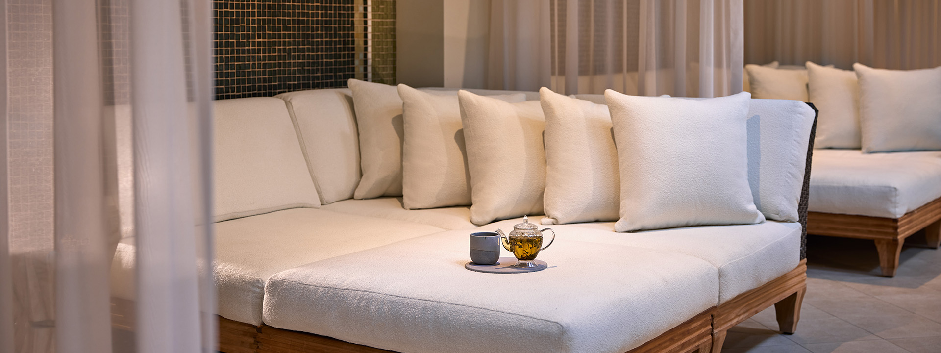 Couch adorned with a charming kettle, cup, and tray invites elegant relaxation and comfort.
