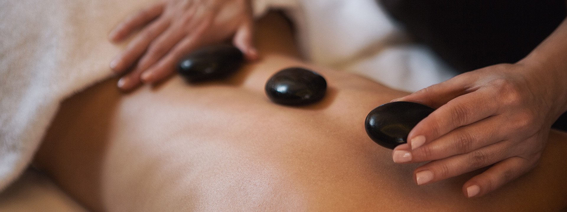 Three hot stones being placed on a woman's back during a spa treatment.