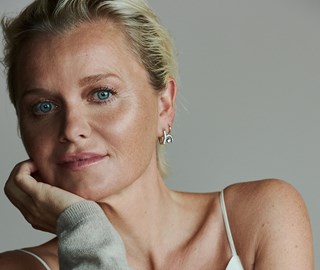 A photo of a blond woman with blue eyes looking at the camera with a grey background.