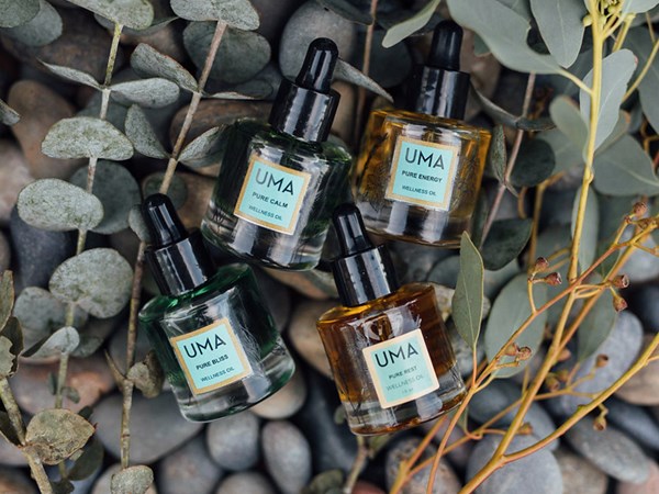 Four bottles of Uma brand wellness oil laying on rocks and vines.