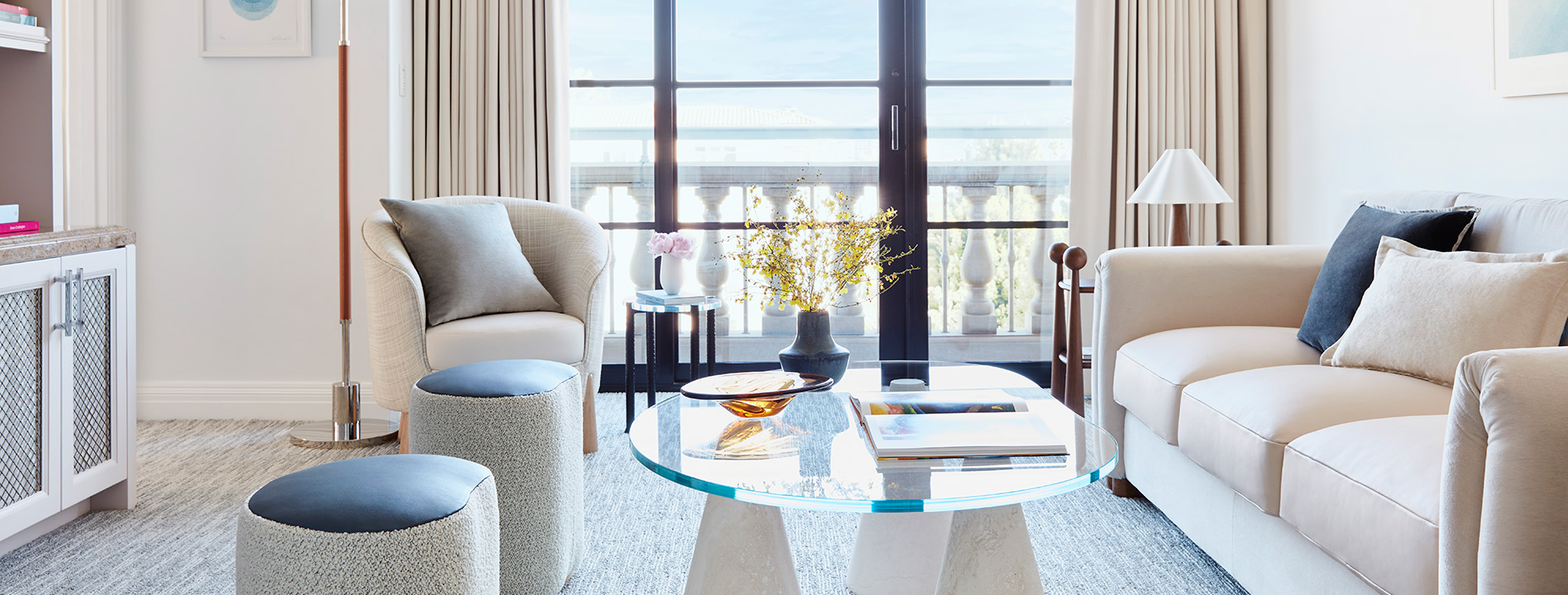 An elegant sofa is placed by the glass window, with a matching glass coffee table.