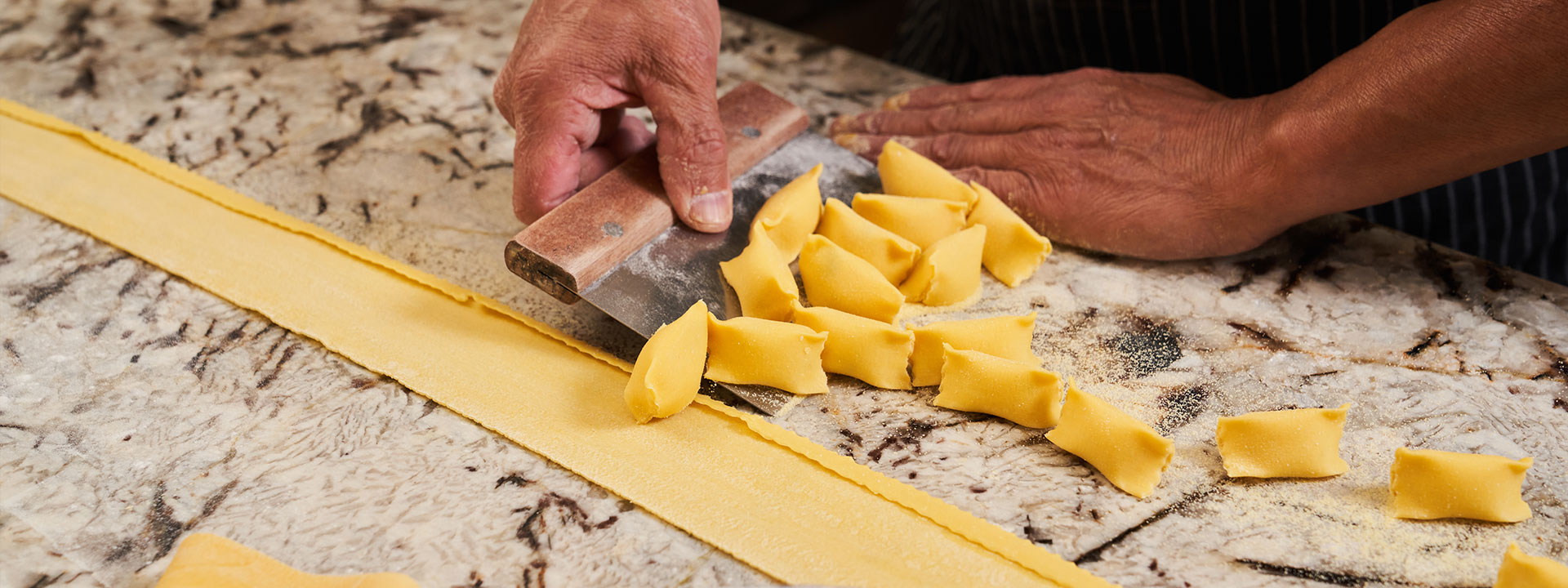 Man rolling pasta out on marble countertop