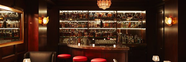 A dimly lit wooden bar with red stools and shelves of whisky bottles.