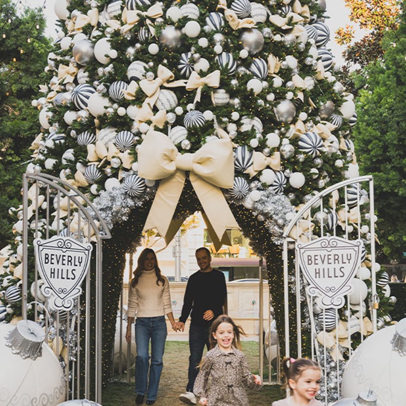 A festive entrance in Beverly Hills featuring a towering Christmas tree decorated with elegant bows and ornaments, flanked by smiling children and parents.